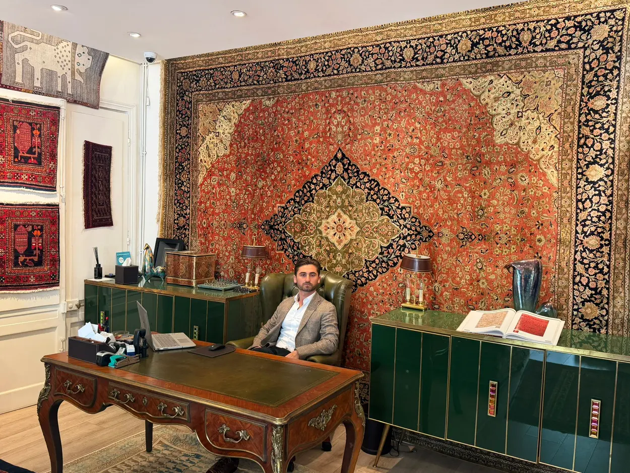 Le responsable de l'atelier dans le showroom, devant un grand tapis Tabriz ancien